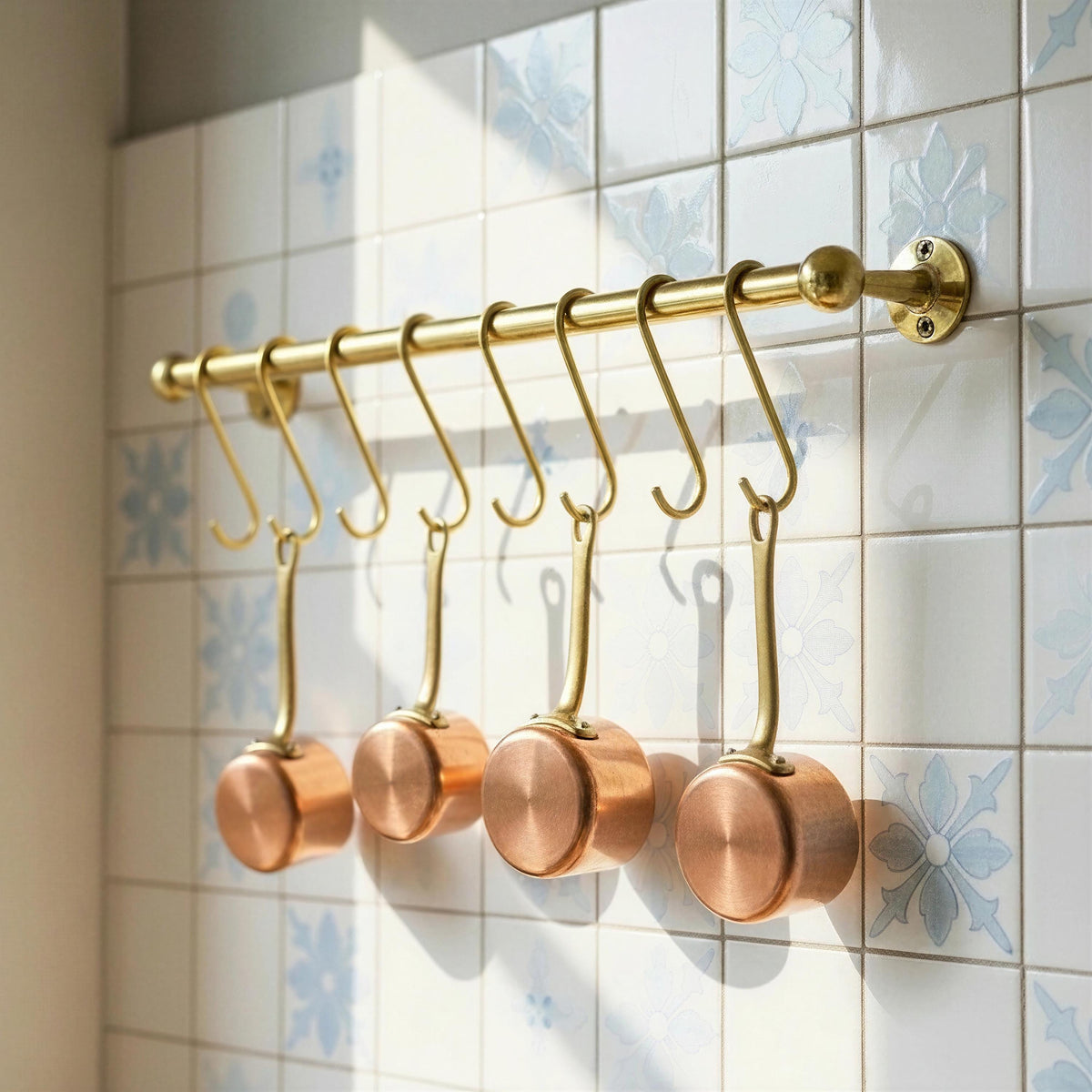Handmade brass kitchen pot rail with S hooks and copper pans against patterned tiles